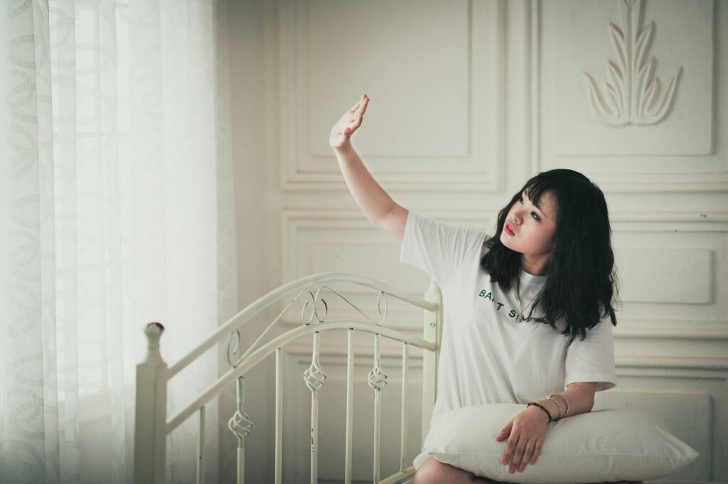 Woman enjoying sunlight in a cozy bedroom setting, expressing relaxation and peace.